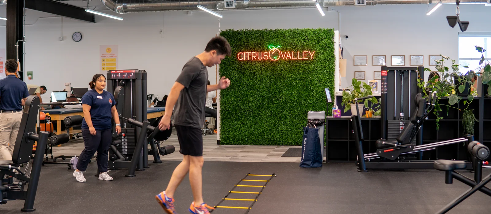 Patient doing agility ladder drills on the Citrus Valley gym floor while staff work nearby