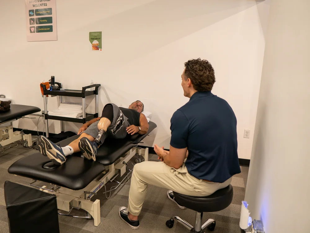 Physical therapist seated beside a patient lying on a treatment table